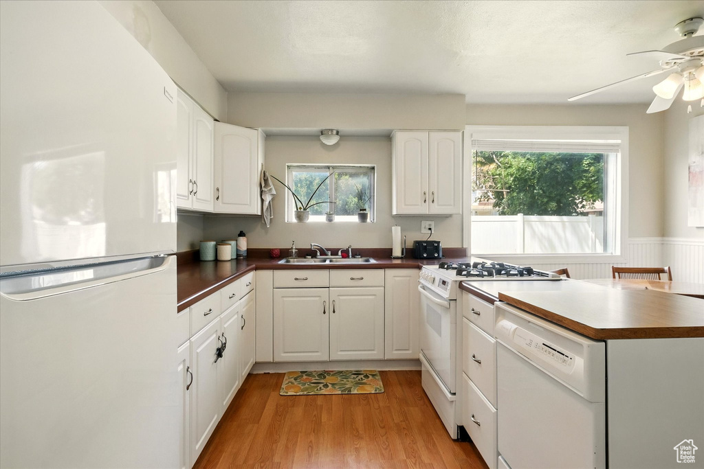 Kitchen featuring white appliances, dark countertops, ceiling fan, light wood finished floors, and white cabinets