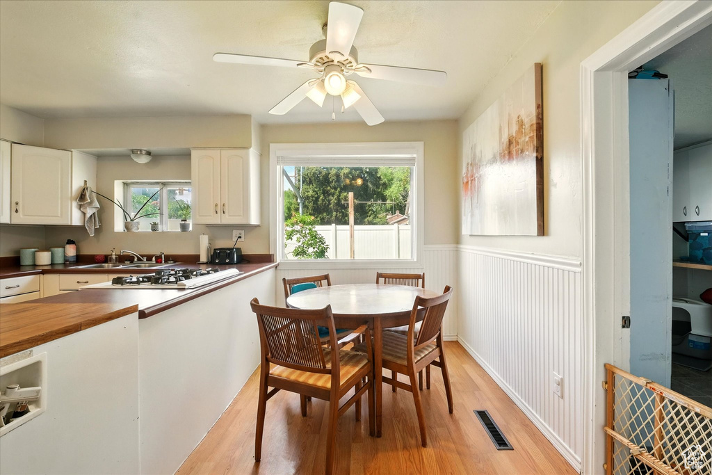 Dining room with light wood-type flooring, a wainscoted wall, and ceiling fan