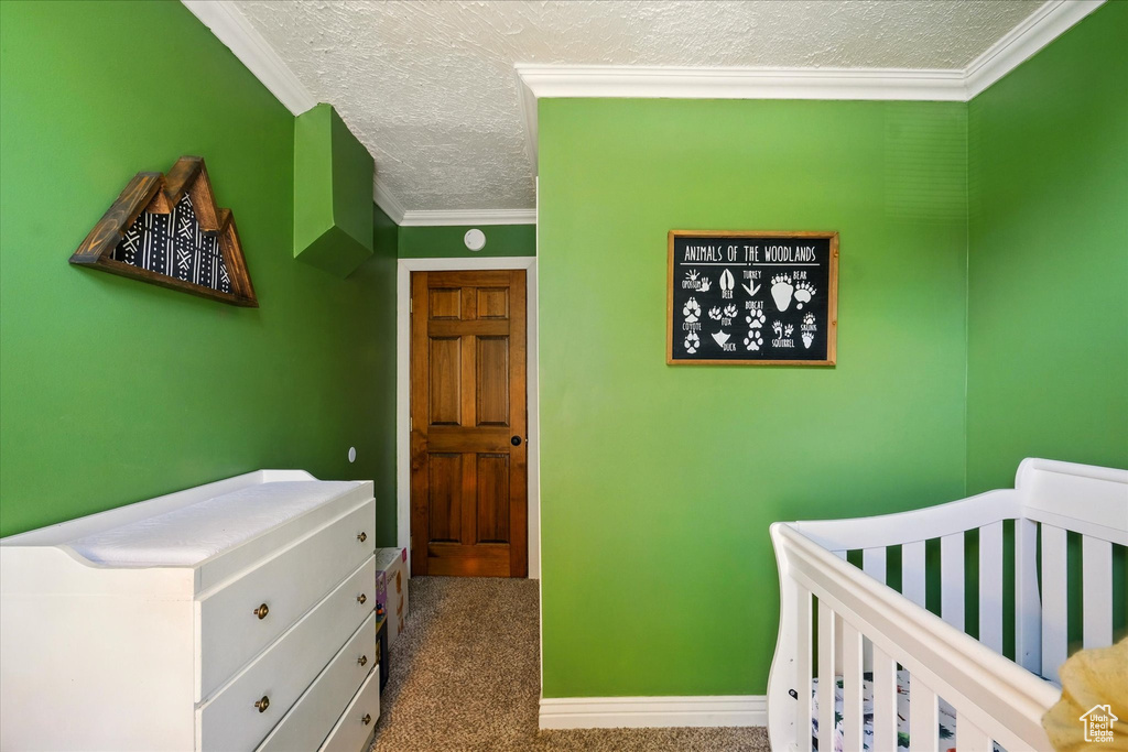 Carpeted bedroom featuring a textured ceiling, ornamental molding, and a nursery area