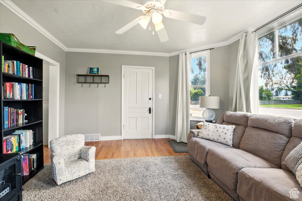 Living room with plenty of natural light, wood finished floors, ceiling fan, and crown molding