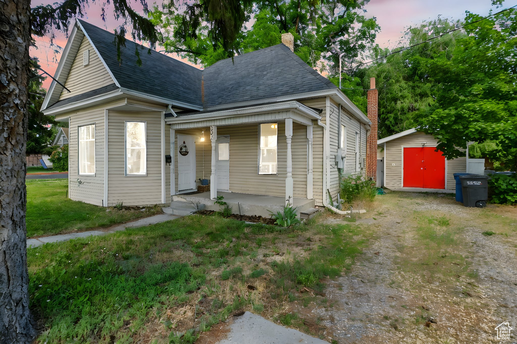 View of front of property with covered porch, a storage shed, roof with shingles, a chimney, and a yard