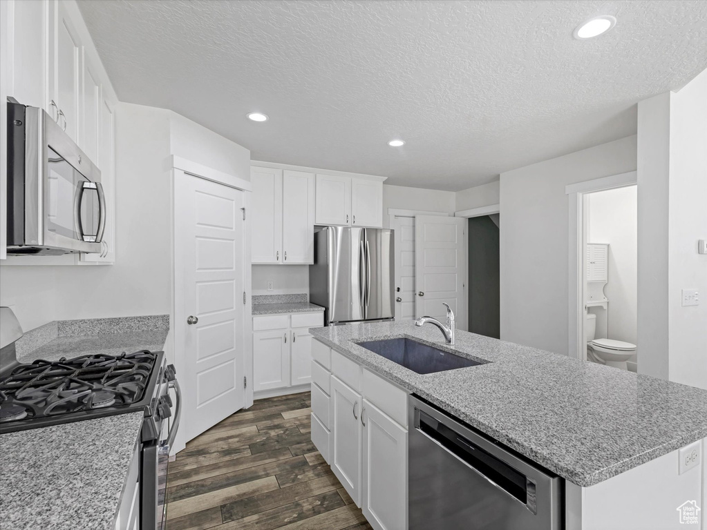 Kitchen featuring stainless steel appliances, dark wood-style floors, a textured ceiling, an island with sink, and white cabinets