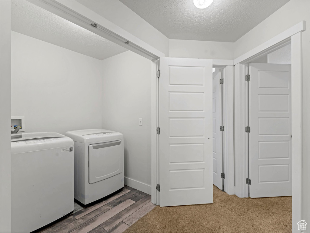 Washroom with washing machine and dryer, a textured ceiling, and wood finished floors