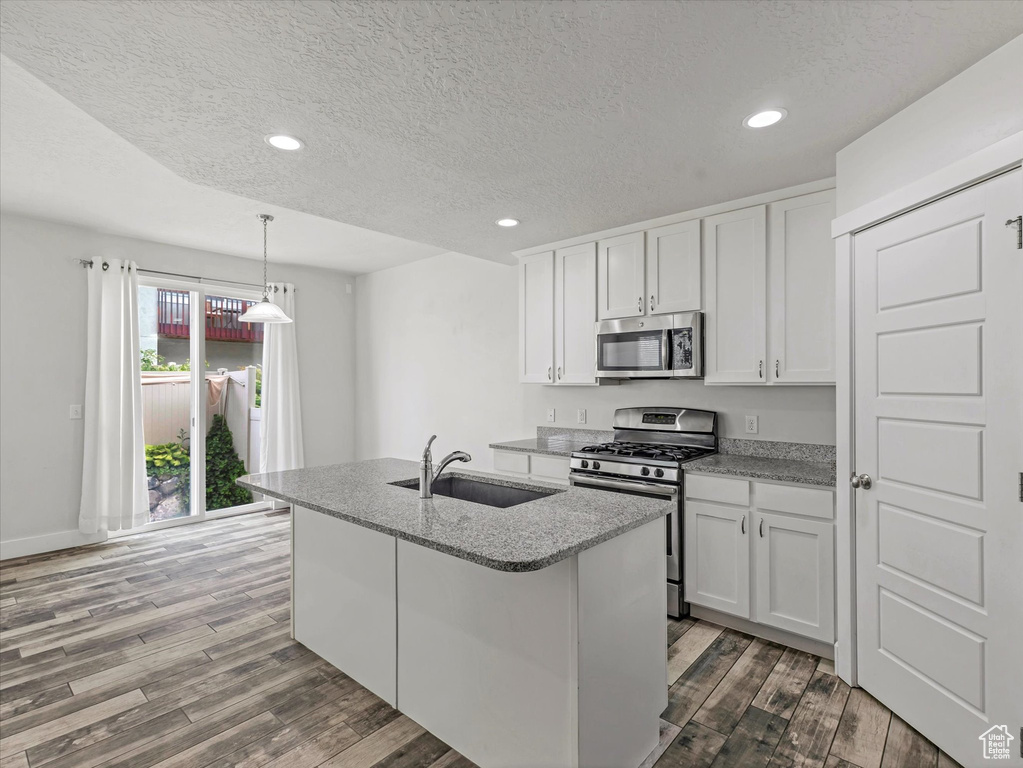 Kitchen with stainless steel appliances, a textured ceiling, dark wood-type flooring, a center island with sink, and white cabinets