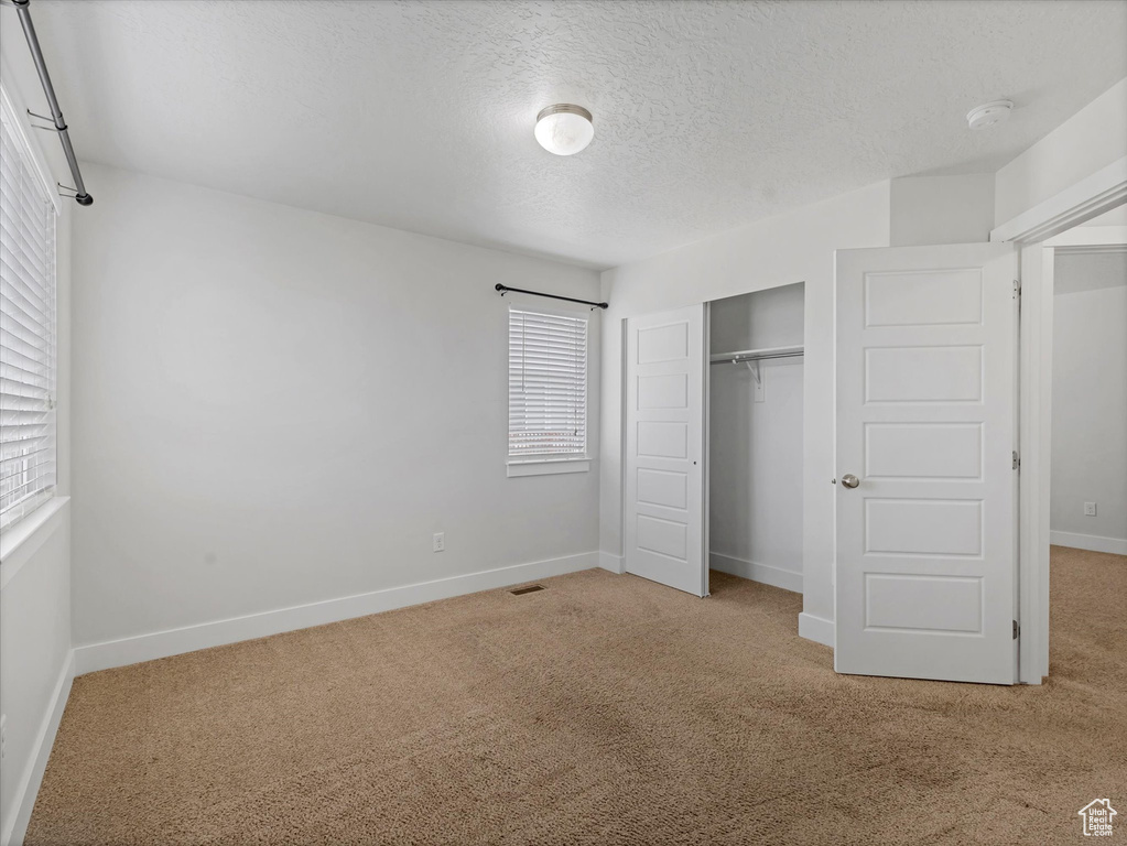 Unfurnished bedroom with carpet, multiple windows, a closet, and a textured ceiling