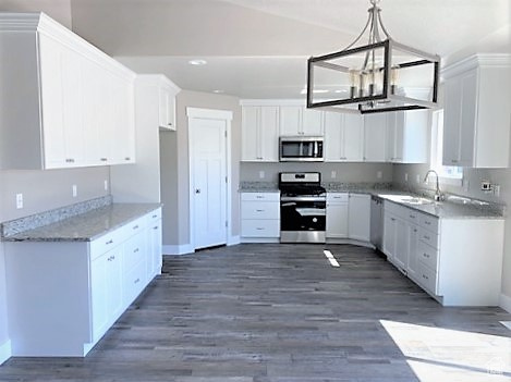 Kitchen featuring appliances with stainless steel finishes, white cabinets, a chandelier, dark wood finished floors, and pendant lighting