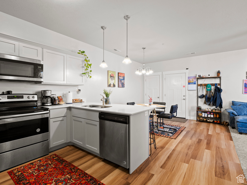 Kitchen featuring stainless steel appliances, light wood-style floors, a chandelier, a peninsula, and light countertops