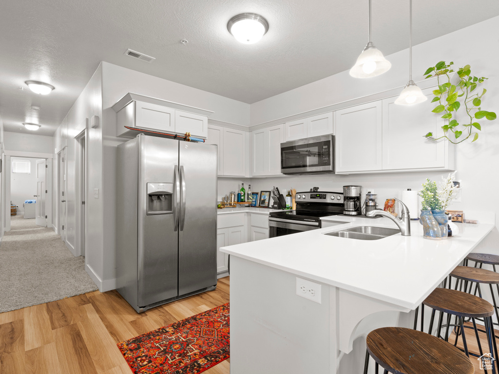 Kitchen featuring stainless steel appliances, a peninsula, light wood-style flooring, a breakfast bar, and light countertops