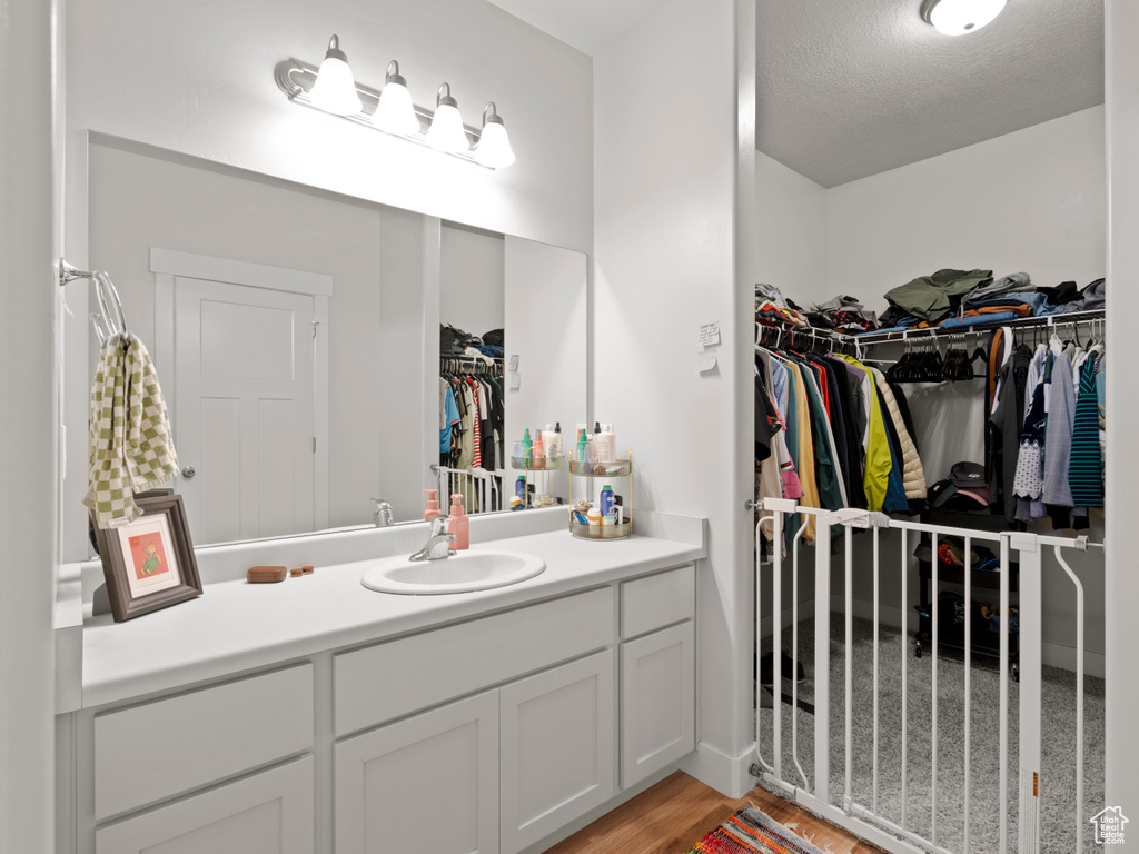 Bathroom with vanity, wood finished floors, a spacious closet, and a textured ceiling