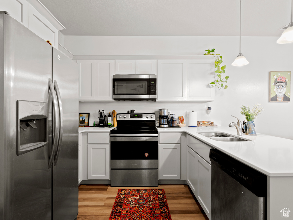 Kitchen with stainless steel appliances, a peninsula, light countertops, light wood-type flooring, and hanging light fixtures