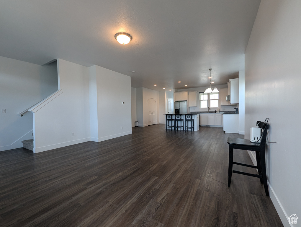 Unfurnished living room featuring dark wood-style floors, baseboards, stairway, a chandelier, and a sink