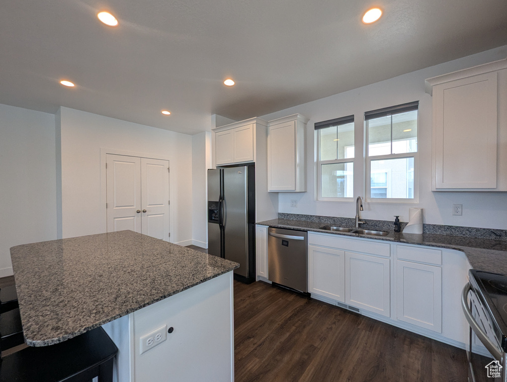 Kitchen featuring appliances with stainless steel finishes, a sink, dark wood finished floors, white cabinetry, and dark stone counters