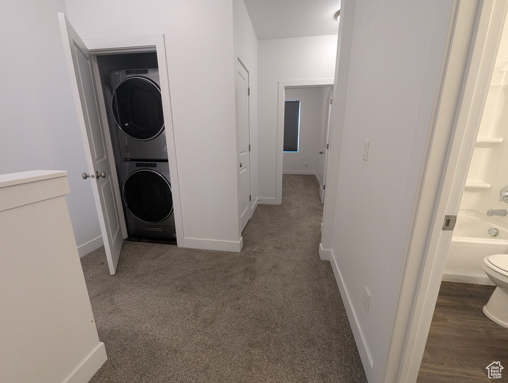 Laundry room with stacked washing machine and dryer, baseboards, and carpet