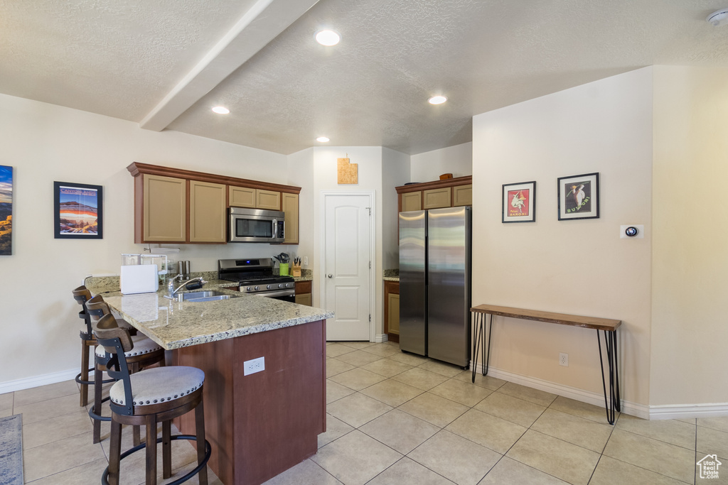 Kitchen with stainless steel appliances, a peninsula, a textured ceiling, a breakfast bar area, and light tile patterned floors