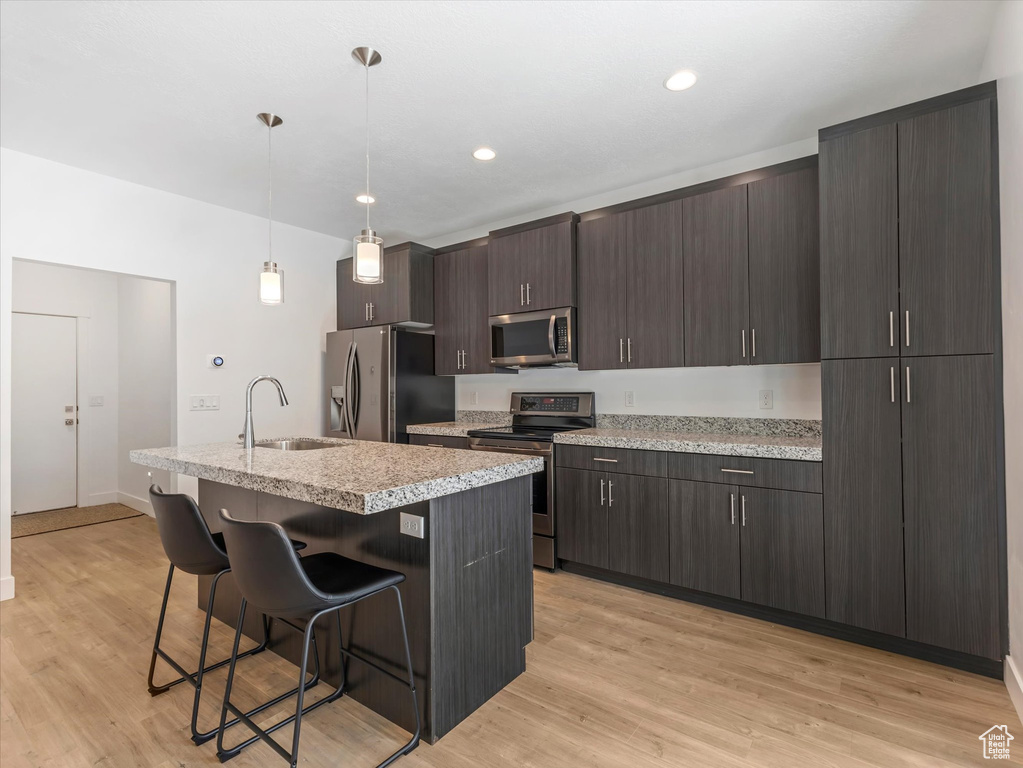 Kitchen featuring stainless steel appliances, a breakfast bar area, a kitchen island with sink, light wood-style flooring, and dark brown cabinets