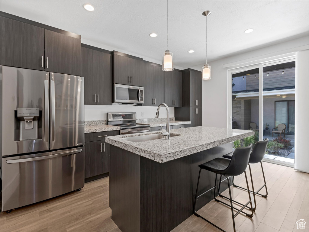 Kitchen with appliances with stainless steel finishes, light countertops, light wood-style floors, a breakfast bar area, and recessed lighting