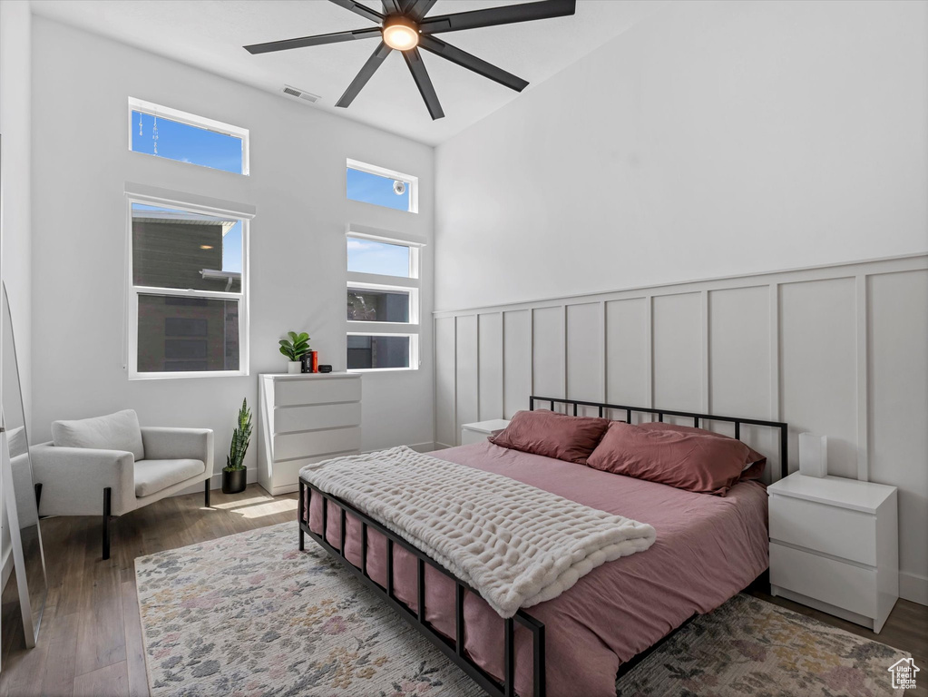 Bedroom featuring wood finished floors, ceiling fan, a wainscoted wall, a towering ceiling, and a decorative wall