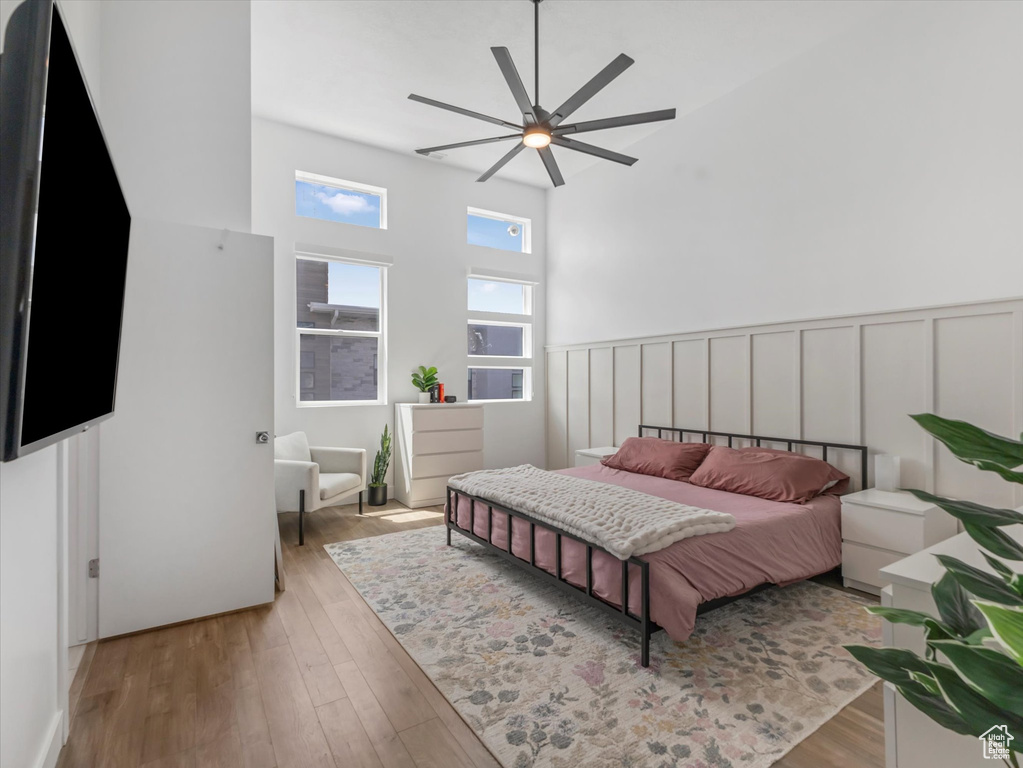 Bedroom featuring wood finished floors, a wainscoted wall, a decorative wall, a towering ceiling, and ceiling fan