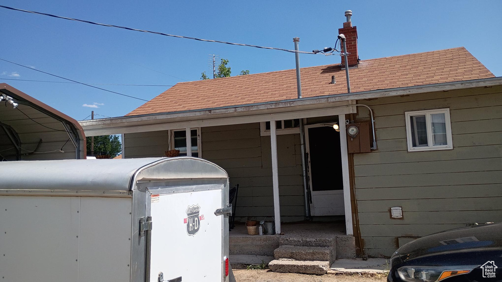 Exterior space featuring a shingled roof, a chimney, and a detached carport