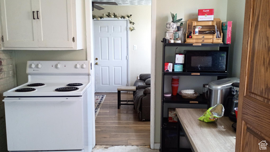 Kitchen with white electric stove, black microwave, white cabinets, light wood-style flooring, and ceiling fan