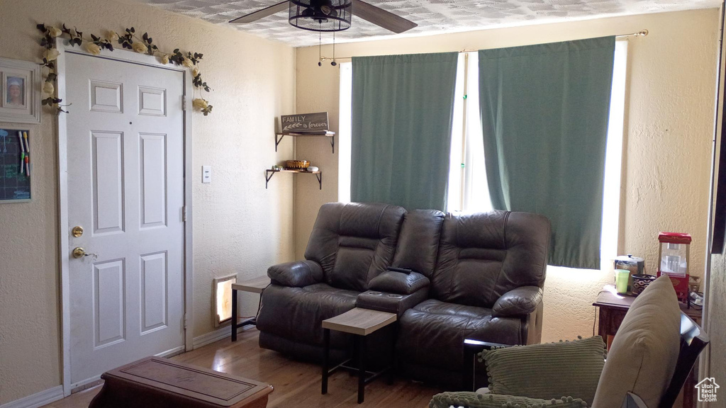 Living area with a ceiling fan, wood finished floors, and a textured wall
