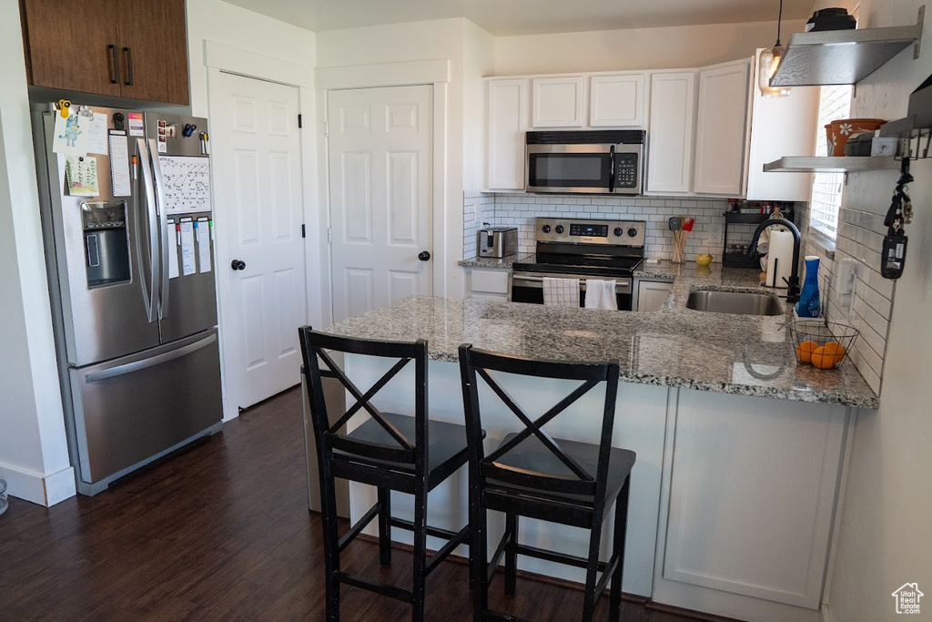 Kitchen with stainless steel appliances, a peninsula, backsplash, white cabinetry, and dark wood finished floors