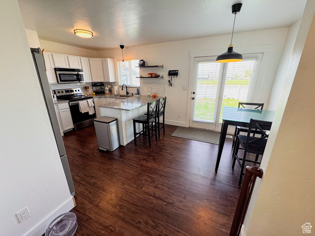 Kitchen featuring appliances with stainless steel finishes, dark wood-style floors, a kitchen bar, pendant lighting, and a peninsula