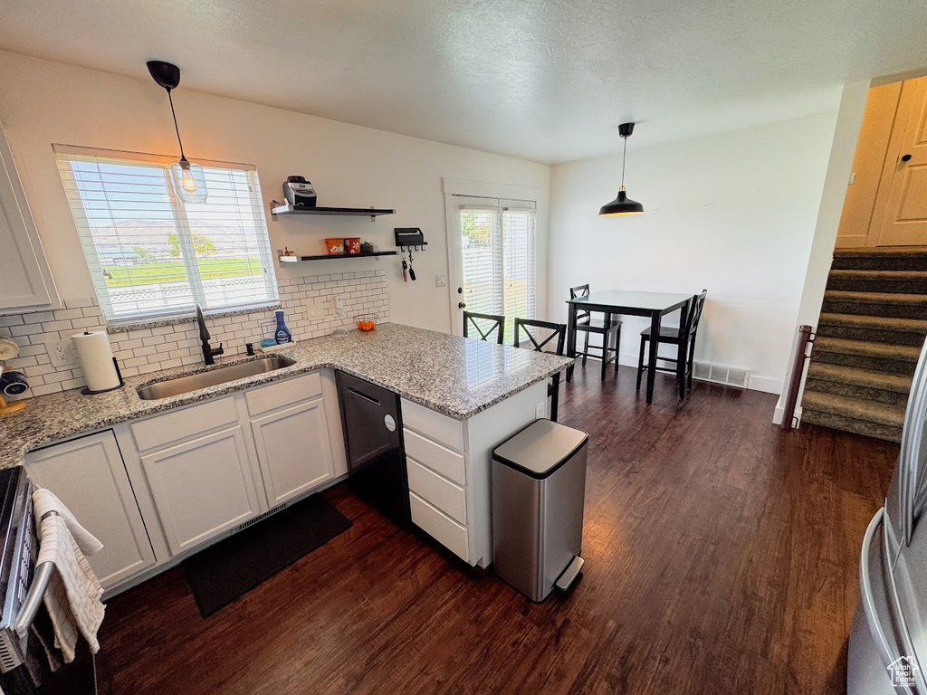 Kitchen with black dishwasher, dark wood finished floors, a peninsula, and tasteful backsplash