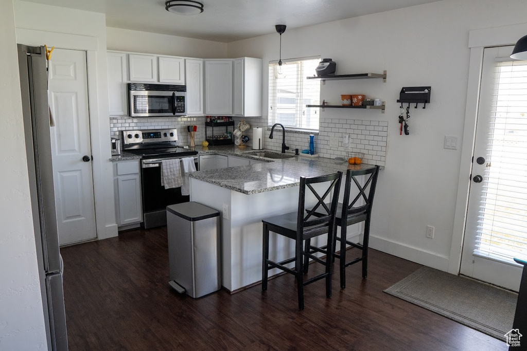 Kitchen featuring appliances with stainless steel finishes, a peninsula, dark wood finished floors, backsplash, and light stone counters
