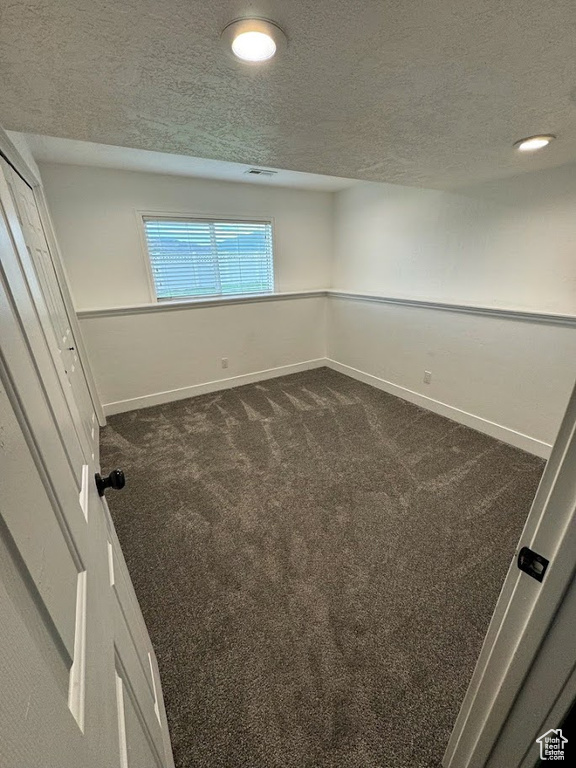Unfurnished room featuring dark colored carpet and a textured ceiling