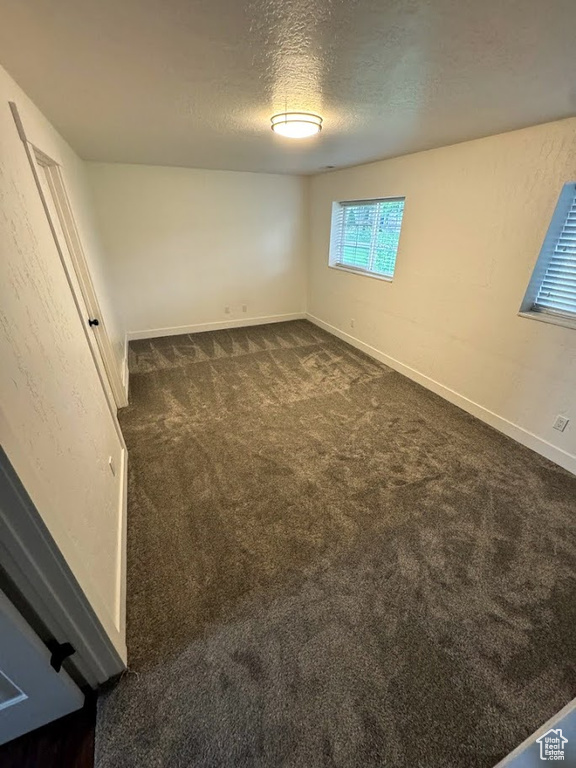 Unfurnished room with dark carpet and a textured ceiling