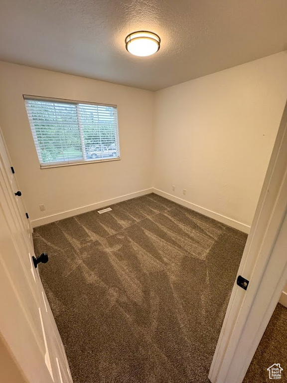 Empty room featuring dark carpet and a textured ceiling