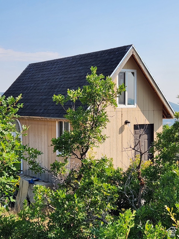 View of side of home with a shingled roof and a storage unit