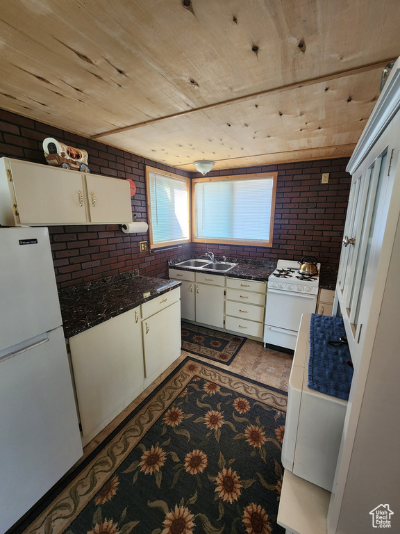 Kitchen featuring white appliances, brick wall, dark countertops, wood ceiling, and white cabinets