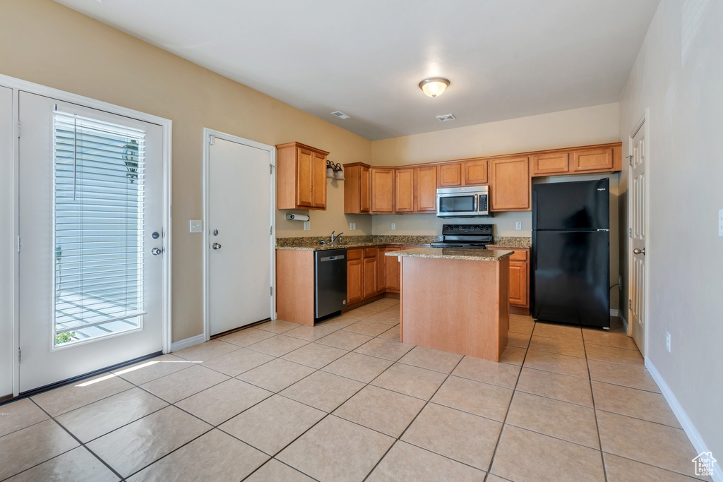 Kitchen with black appliances, light stone counters, light tile patterned floors, and a kitchen island