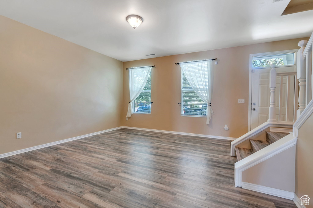 Empty room with stairs, plenty of natural light, and wood finished floors
