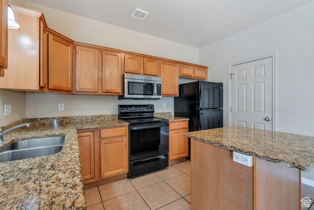 Kitchen featuring black appliances, light tile patterned flooring, light stone counters, and a kitchen island