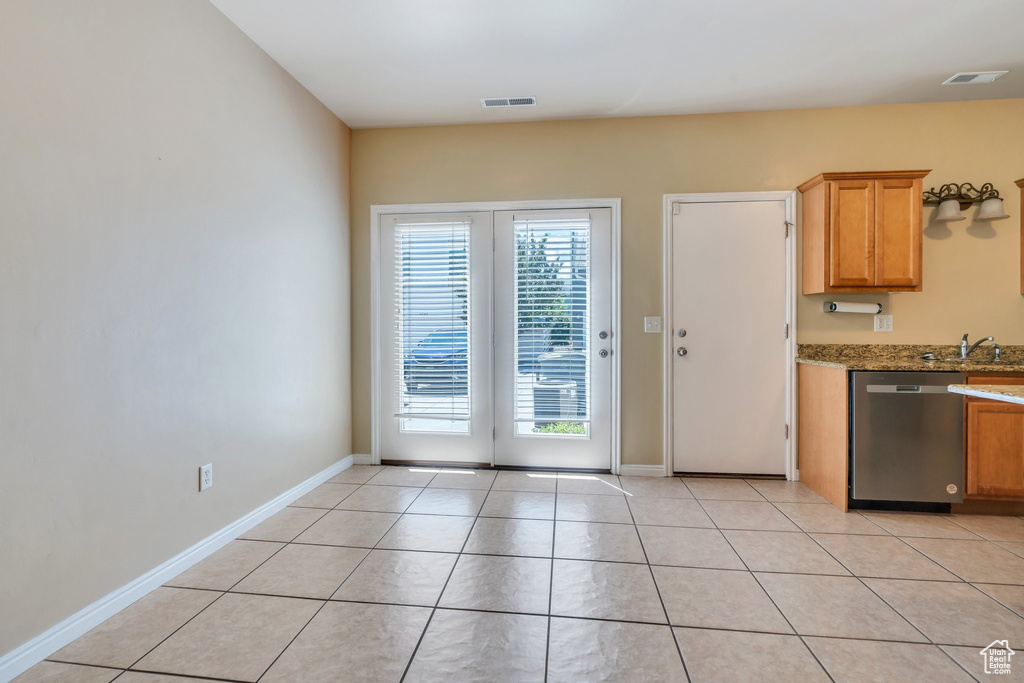 Kitchen with stainless steel dishwasher, stone countertops, and light tile patterned flooring