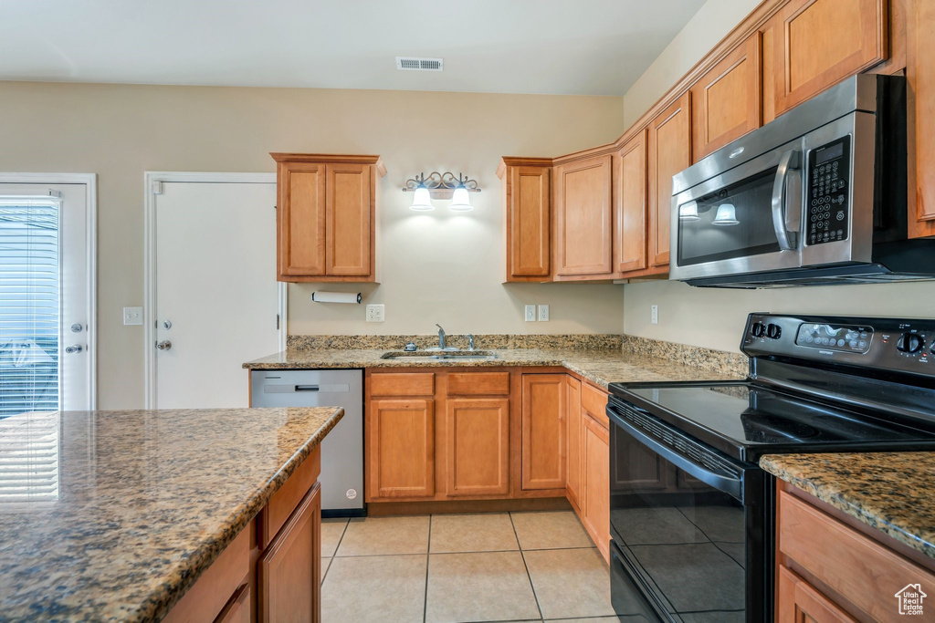 Kitchen featuring stainless steel appliances, light tile patterned flooring, and dark stone counters