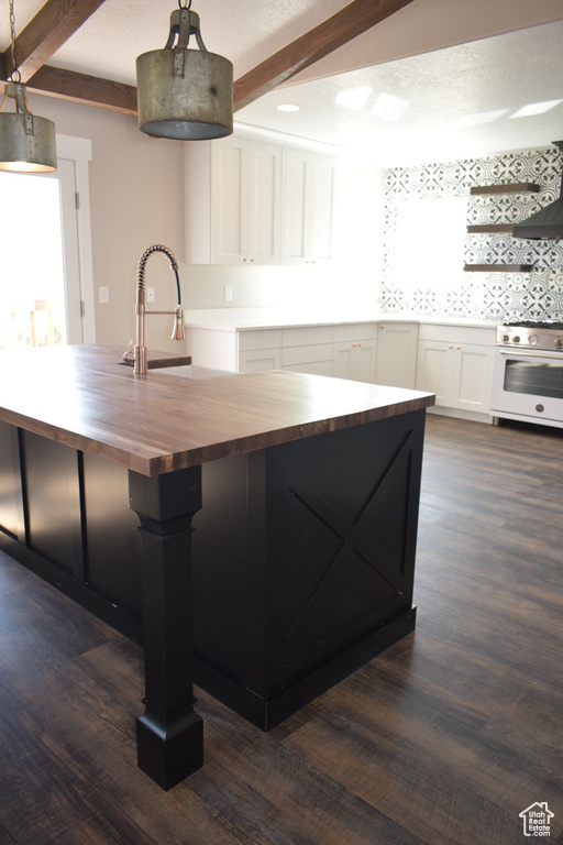 Kitchen with butcher block countertops, high end stainless steel range oven, beam ceiling, dark wood finished floors, and white cabinetry