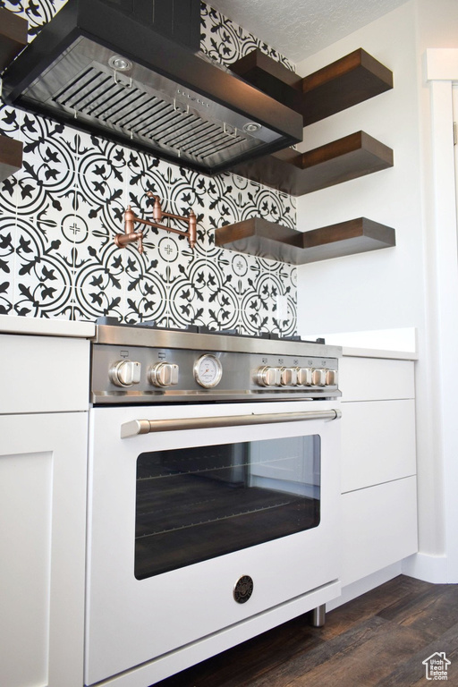 Kitchen view of extractor fan, pot filler, dark wood finished floors, high end white range oven, and white cabinetry