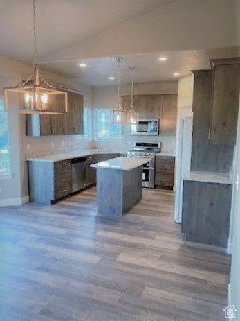 Kitchen featuring appliances with stainless steel finishes, vaulted ceiling, a center island, light wood finished floors, and light countertops