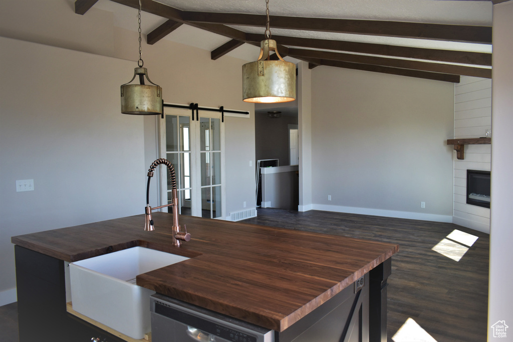 Kitchen with butcher block counters, dishwashing machine, a barn door, dark wood-type flooring, and a fireplace