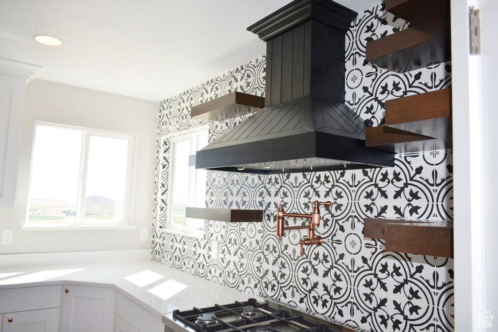 Kitchen with open shelves, wall chimney range hood, light countertops, and stainless steel gas cooktop