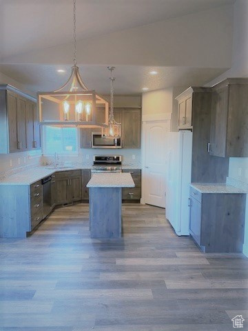 Kitchen featuring stainless steel appliances, lofted ceiling, wood finished floors, a kitchen island, and light countertops