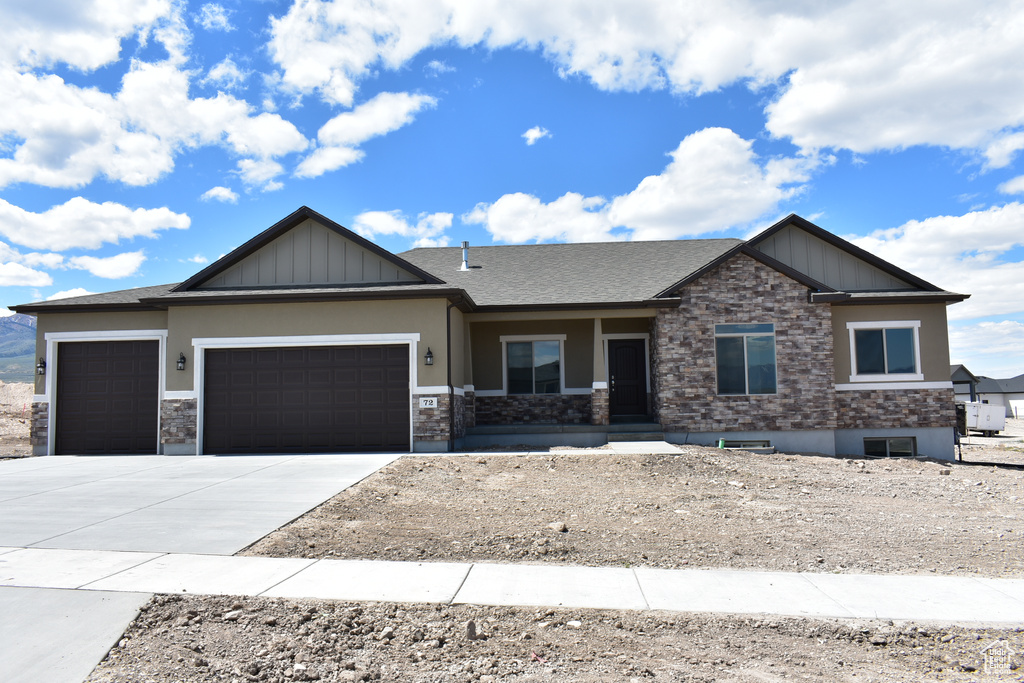 Craftsman inspired home featuring an attached garage, stone siding, driveway, and board and batten siding