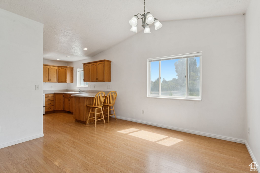Kitchen featuring a chandelier, light wood-style flooring, a breakfast bar, light countertops, and a peninsula
