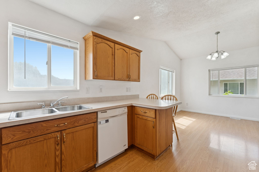 Kitchen with dishwasher, a peninsula, light wood-style flooring, light countertops, and vaulted ceiling
