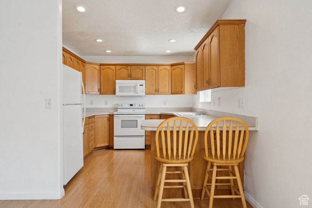 Kitchen with white appliances, a peninsula, light wood-style flooring, recessed lighting, and light countertops