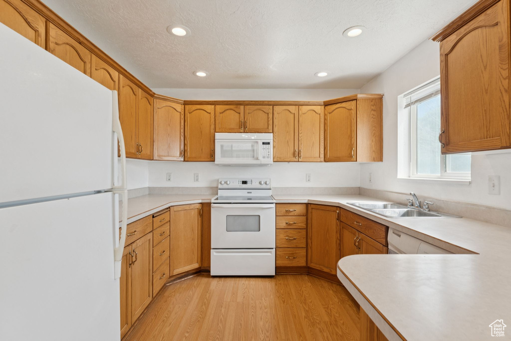 Kitchen with white appliances, light wood-type flooring, recessed lighting, light countertops, and brown cabinets